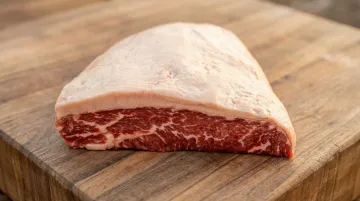 Well-marbled whole picanha cut with thick intact fat cap on butcher block