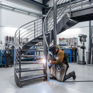 Craftsman fabricating custom metal staircase in professional workshop
