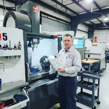 CNC machinist reviewing a precision part at a 5 axis machining center