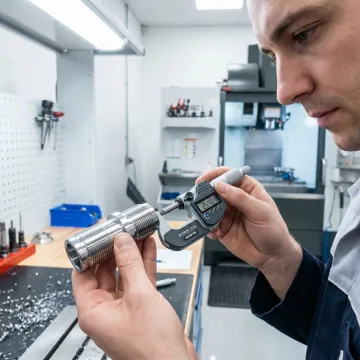 Machinist inspecting a precision CNC turned metal part with measuring tools
