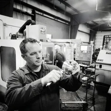 Machinist reviewing a precision metal part at a CNC workstation in a manufacturing shop