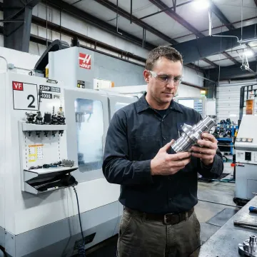 CNC machinist inspecting a precision-machined metal component in a modern machine shop