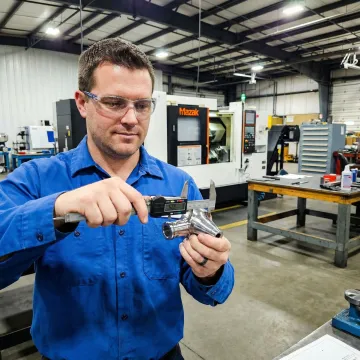 Machinist inspecting precision-manufactured metal part using measurement tools in a CNC machine shop