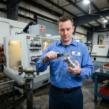 Machinist inspecting a precision-turned metal part for quality assurance in a manufacturing facility