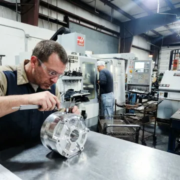 CNC machinist reviewing aluminum part during inspection in a precision machine shop