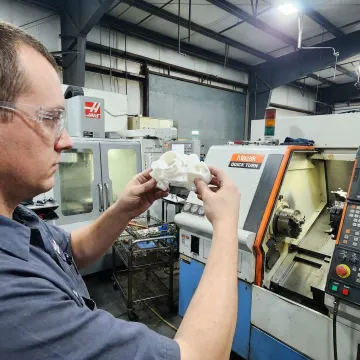 Machinist inspecting a custom plastic precision part on a CNC machine