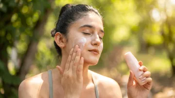 Woman applying broad spectrum sunscreen outdoors under bright sunlight for skin protection