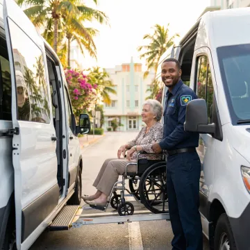 Caring medical transport specialist assisting elderly patient into wheelchair van