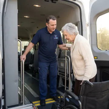 Caring medical transport specialist assisting senior with wheelchair in modern transport vehicle