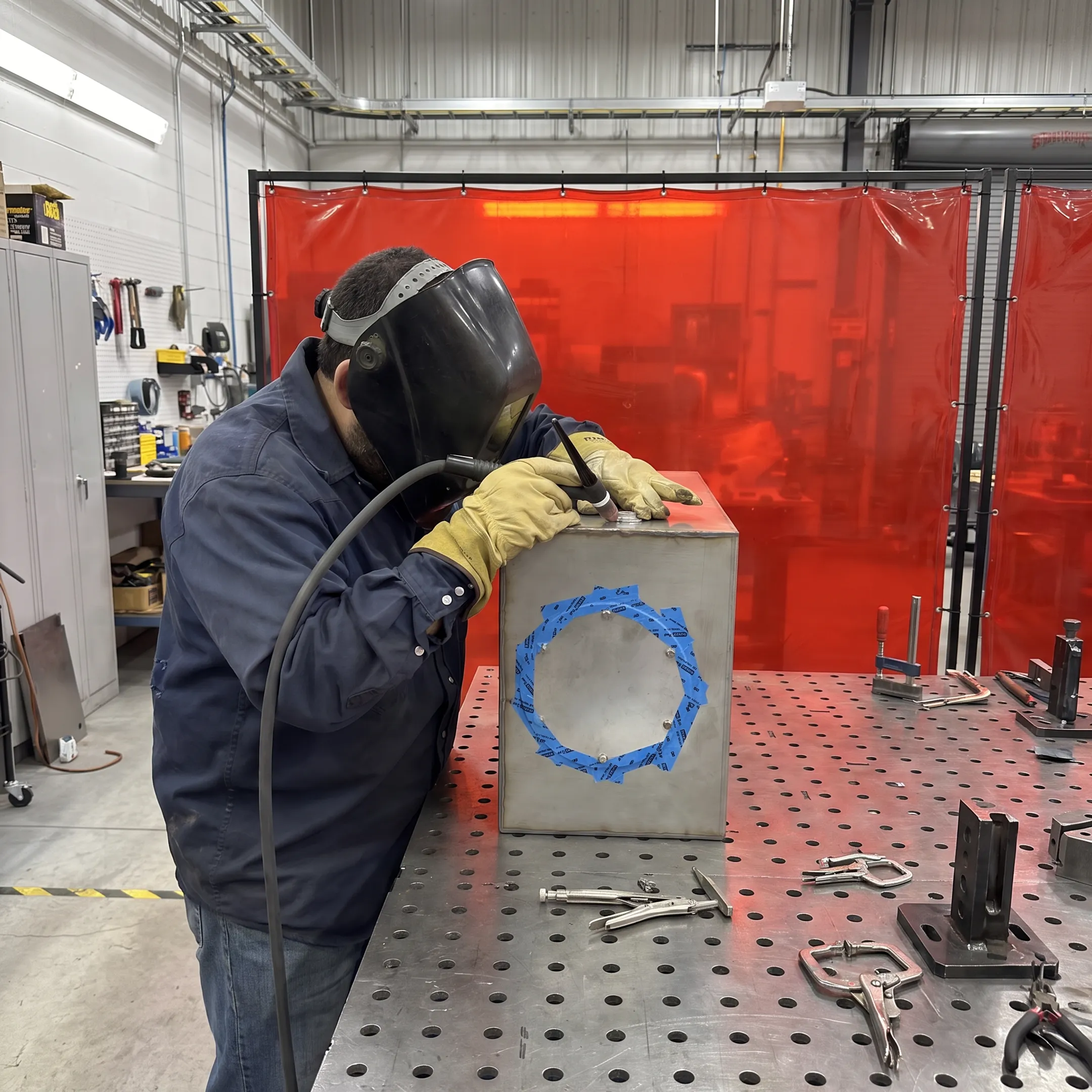 Technician welding a custom metal equipment enclosure in a precision fabrication shop