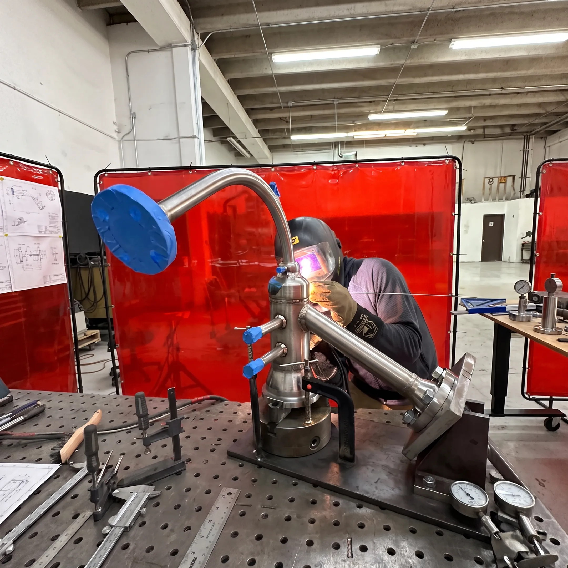 Technician welding a precision metal assembly in a controlled fabrication shop