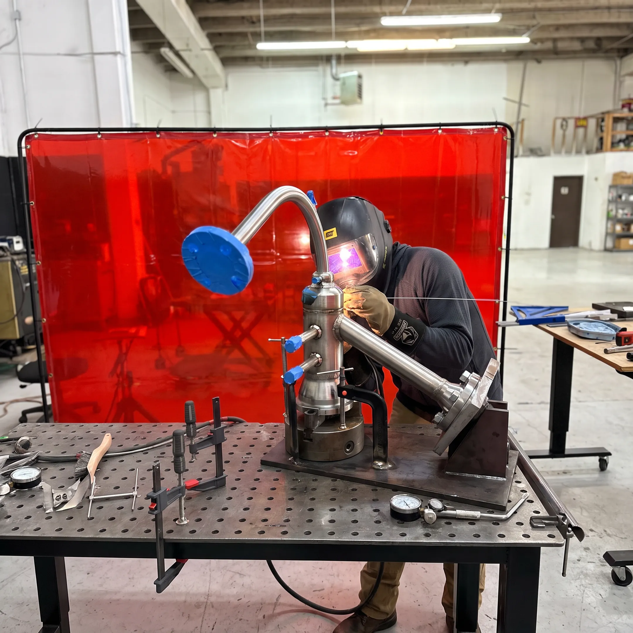 Welder fabricating a precision stainless steel pipe assembly in a controlled workshop