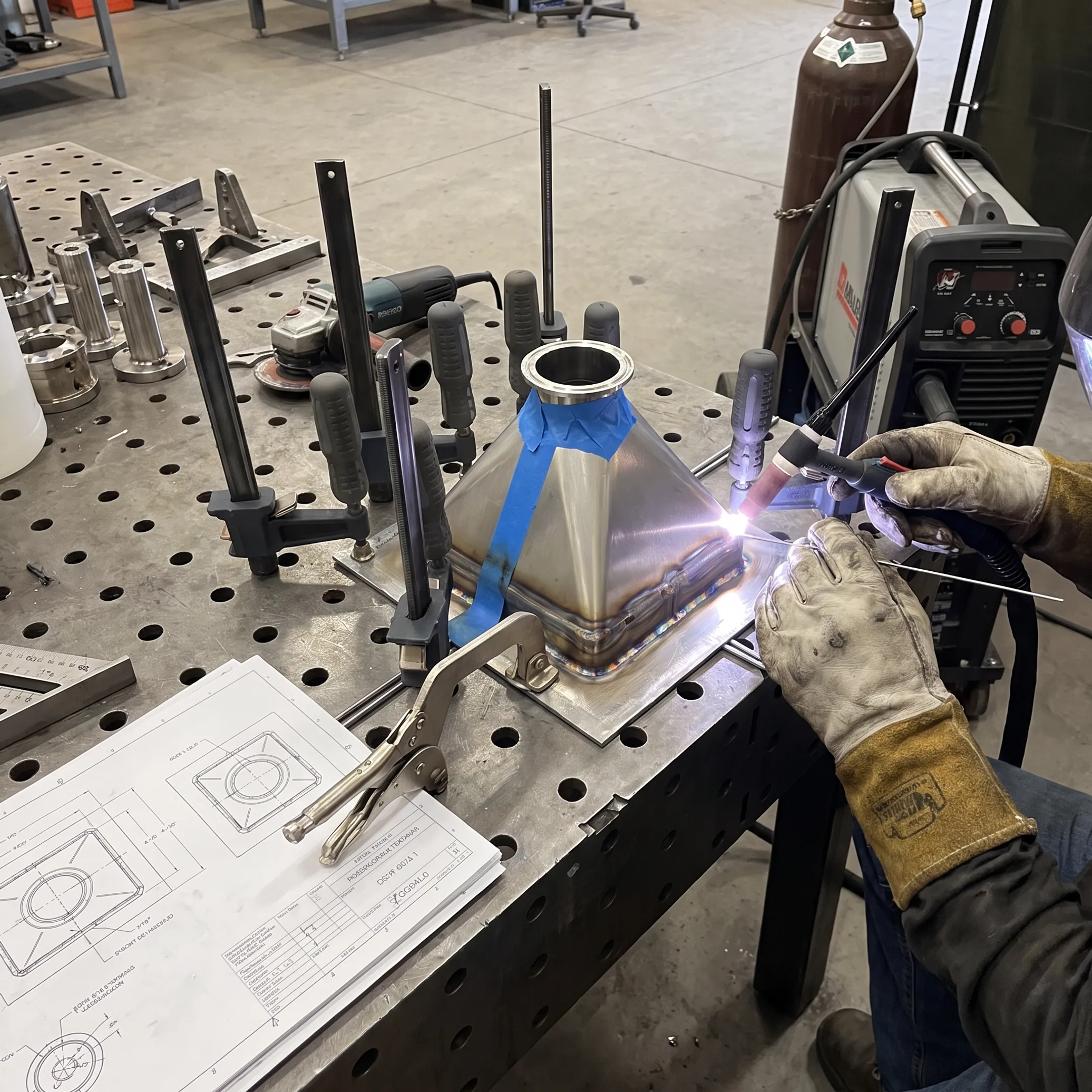 Technician welding a precision prototype assembly in a controlled metal fabrication shop