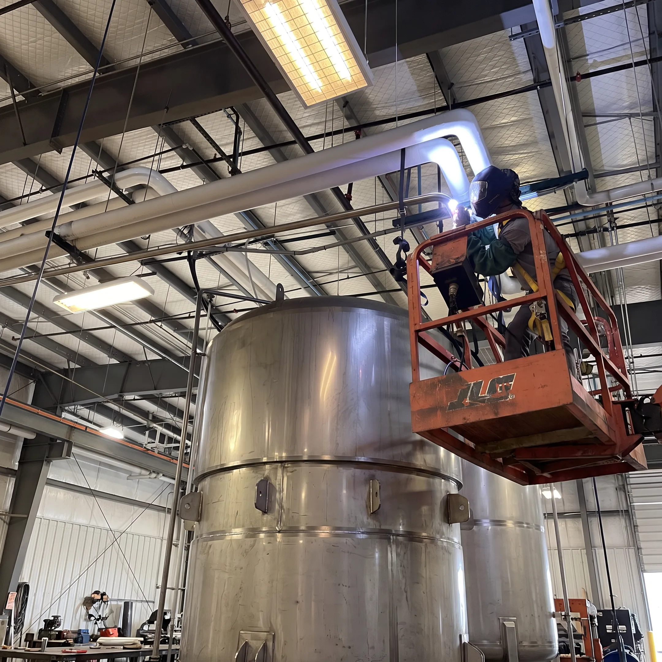 Welder fabricating a chemical storage tank in a precision metalworking shop