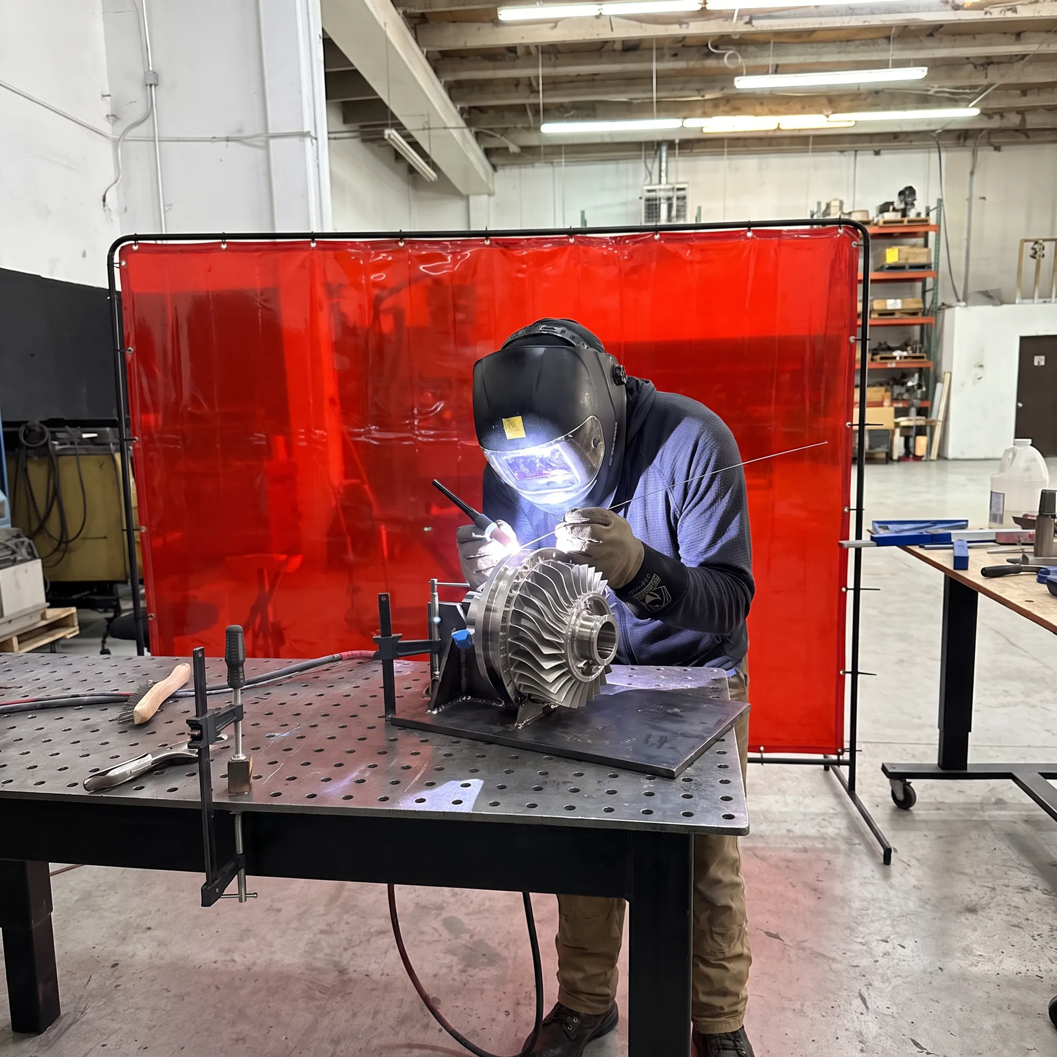 Technician welding a precision turbine component in a controlled fabrication shop