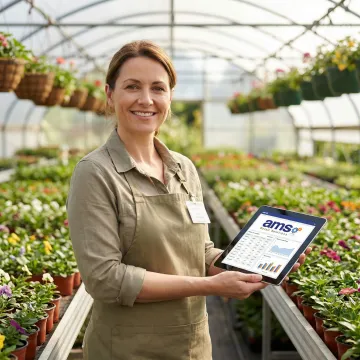 Nursery manager using inventory management software on a tablet among greenhouse plant rows