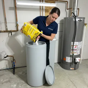 Technician adding salt pellets to a water softener brine tank