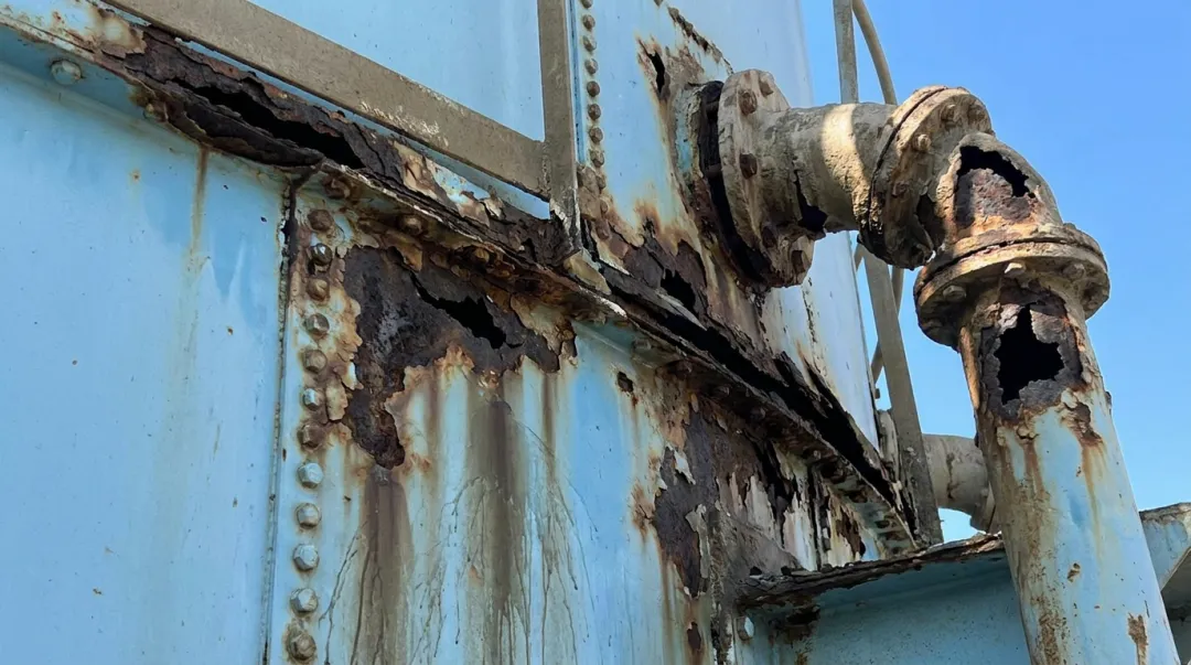 Corroded bolted steel tank panels showing through-wall pitting and structural deterioration