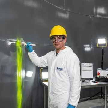 Technician performing ASTM F1929 dye penetration test on industrial tank lining