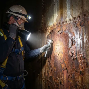Technician inspecting corroded fuel tank interior before relining application
