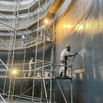 Industrial tank repair crew performing coating application on large steel storage tank