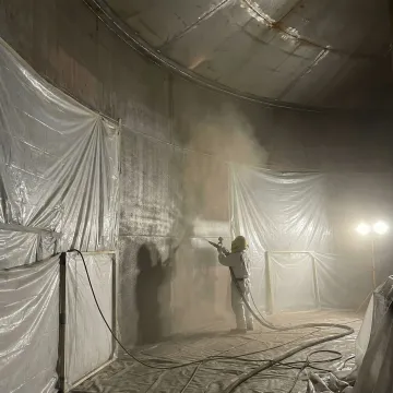 Industrial tank lining specialist performing surface preparation inside large steel storage tank