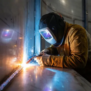Welder performing structural repairs on industrial steel storage tank