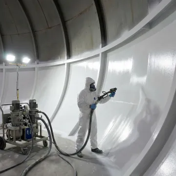 Technician spray-applying protective lining inside commercial grease tank
