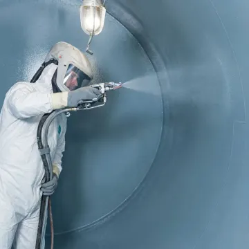 Technician applying industrial tank coating with spray equipment