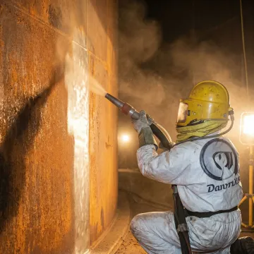 Industrial tank interior being sandblasted by technician in protective gear