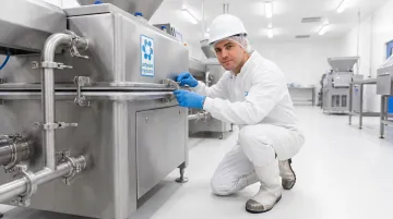 Food processing facility worker inspecting seals on high-speed meat portioning equipment