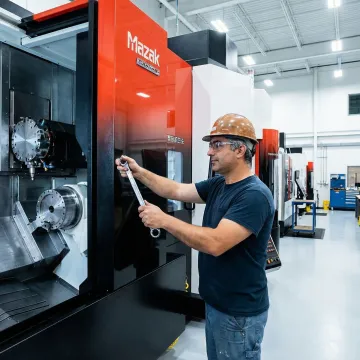 Industrial machinery maintenance technician servicing a CNC machine on a factory floor