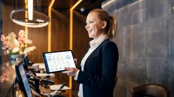 Hotel front desk staff using cloud PMS software on tablet in modern lobby