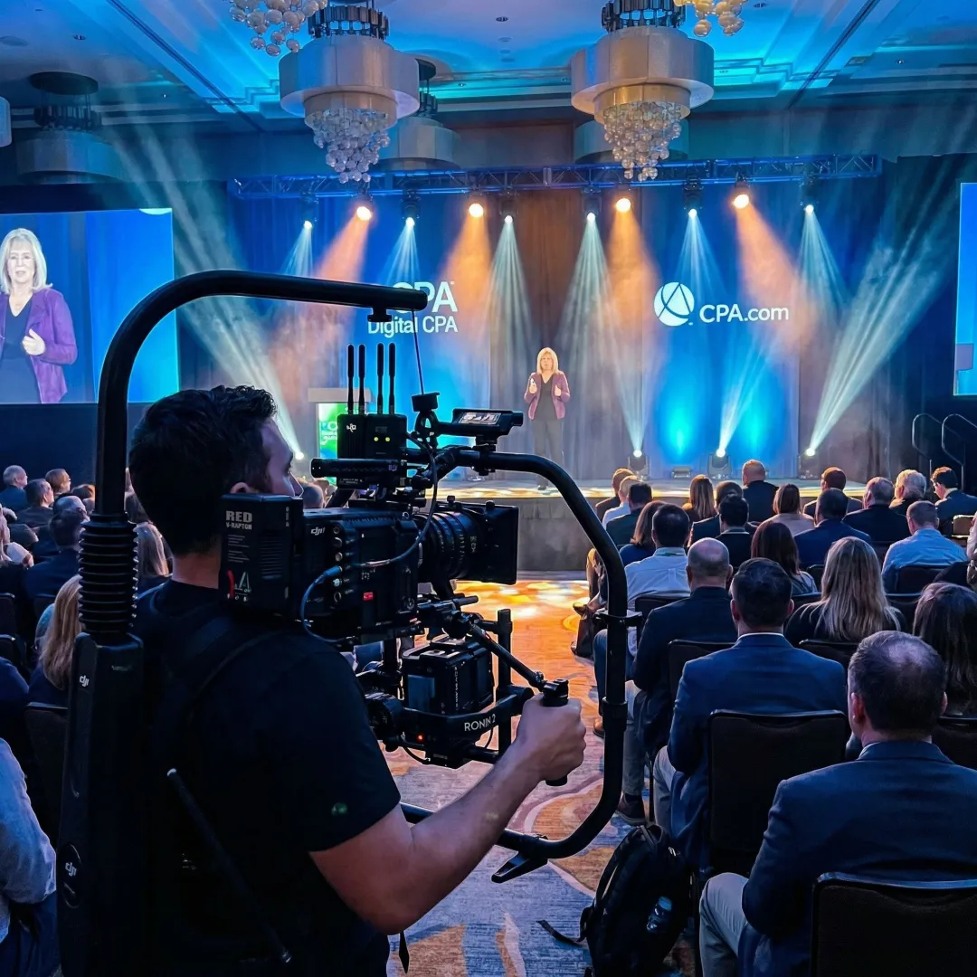 Videographer filming a corporate conference keynote speaker with professional cinema camera