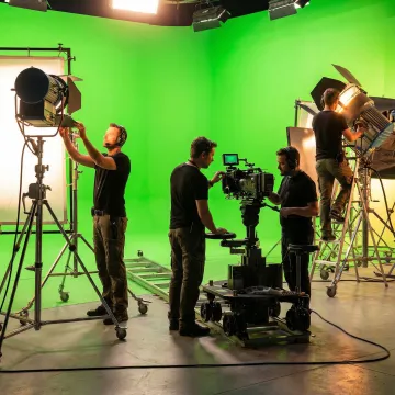 Video production crew setting up green screen lighting and cameras for a studio shoot