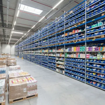 Organized overflow warehouse with stacked inventory pallets and labeled shelving for peak season storage