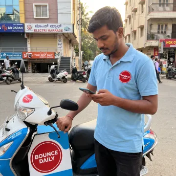 Delivery partner using a smartphone beside an EV scooter