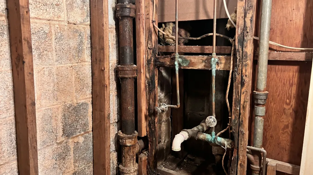 Contractor uncovering water damage and old pipes inside opened bathroom wall during renovation