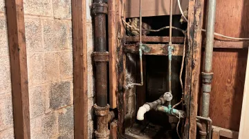 Contractor uncovering water damage and old pipes inside opened bathroom wall during renovation