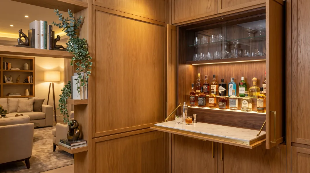 Hidden bookshelf bar cabinet open revealing organized bottle storage glassware and fold-out surface