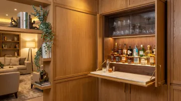 Hidden bookshelf bar cabinet open revealing organized bottle storage glassware and fold-out surface