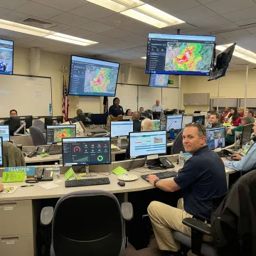 Emergency operations center managing wildfire response with multiple digital displays and coordinated response teams