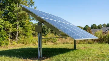 Ground-mounted residential solar panel array installed on open lot beside home