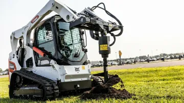 Bobcat compact track loader with hydraulic auger attachment drilling foundation hole on solar site