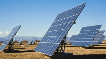 Solar tracking system following sun path across open field with blue sky