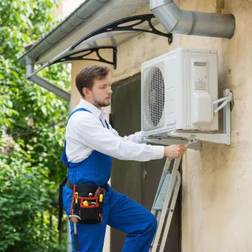 Professional HVAC technician installing ductless mini split system on exterior wall