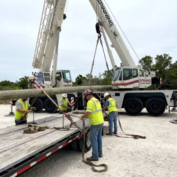 Crane crew preparing utility pole transport