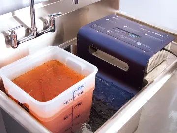 Shallow hotel pans of gravy cooling in an organized commercial kitchen prep area