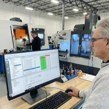 CNC machine shop floor with active machine tools and computer workstation running DNC software