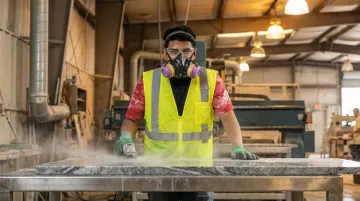 Stone fabrication worker wearing silica dust respiratory protection equipment in shop
